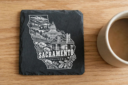 Black slate coaster engraved with a white design of Sacramento California landmarks on a wooden table.
