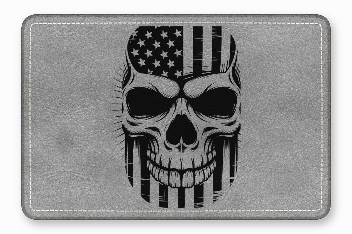 A rectangular grey leather patch featuring a black illustration of a skull superimposed with an American flag.