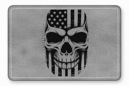A rectangular grey leather patch featuring a black illustration of a skull superimposed with an American flag.