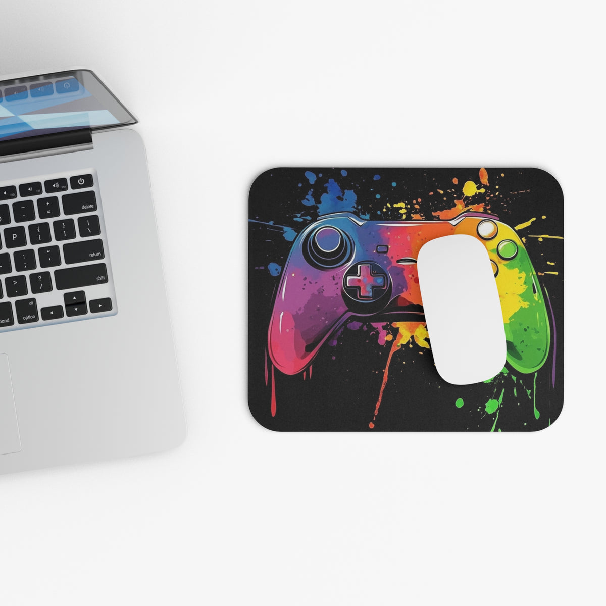 Mousepad with colorful splatter art of a video game controller, next to a laptop.