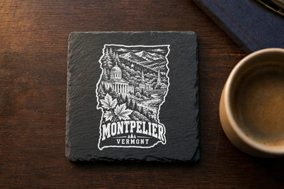 Square black slate coaster engraved with a Vermont state-shaped illustration of Montpelier, maple leaves, and mountains.
