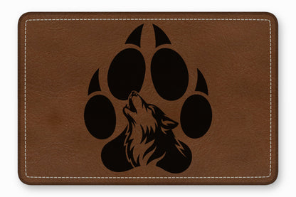 Brown leather patch with rounded corners featuring a black silhouette of a wolf howling inside a paw print.