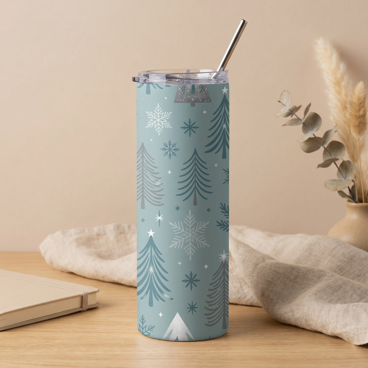 Blue tumbler with white and gray Christmas tree and snowflake pattern and metal straw.