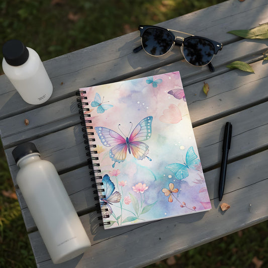 Notebook with watercolor butterflies and flowers on a wooden surface with water bottles and sunglasses.
