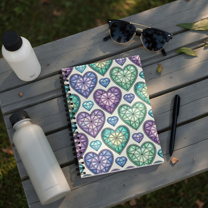 Notebook with gem-like hearts pattern, sunglasses, pen, and two water bottles on a wooden bench.