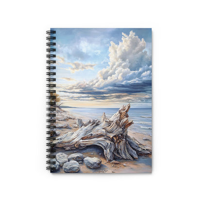 Spiral-bound notebook featuring a painting of driftwood on a sandy beach with a cloudy sky.