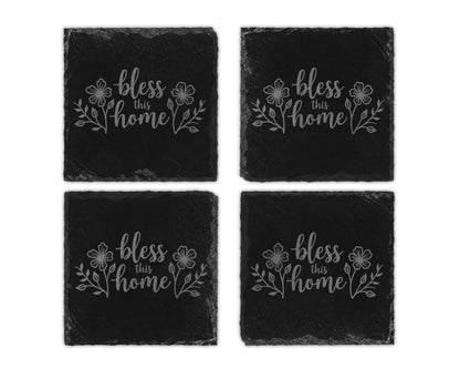 Four black slate coasters with "bless this home" text and floral designs.